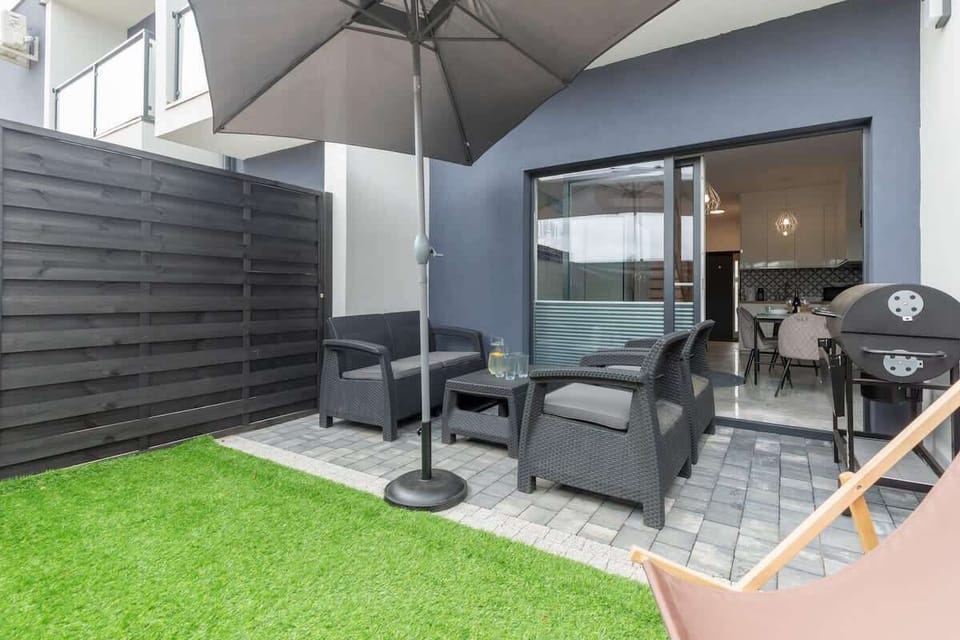 A private patio with outdoor furniture, a green lawn, and umbrellas for enjoying sunny days.