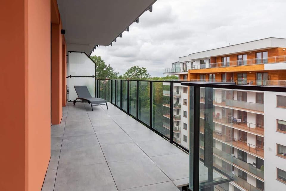 A balcony with a view of the neighborhood, featuring a black railing and space for outdoor seating. The orange exterior adds warmth to the space.