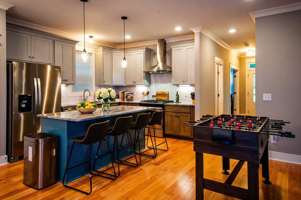 Kitchen island with marble counters and three bar stools becomes command central, foosball games and rounds of drinks never miss a beat with the cook