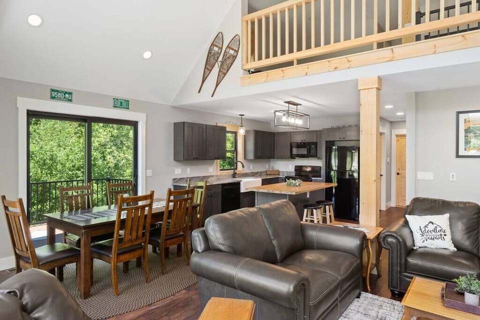 Main living space with vaulted ceilings, open floor plan into the dining and kitchen area, and an incredible wall of windows with views of Mount Snow.