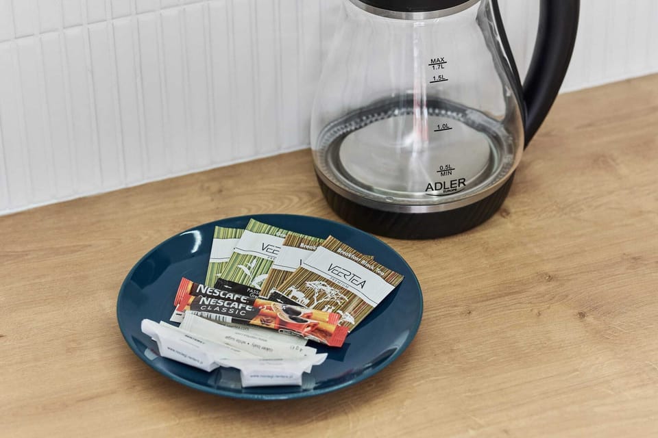 Close-up of electric kettle and plate of tea and coffee sachets.