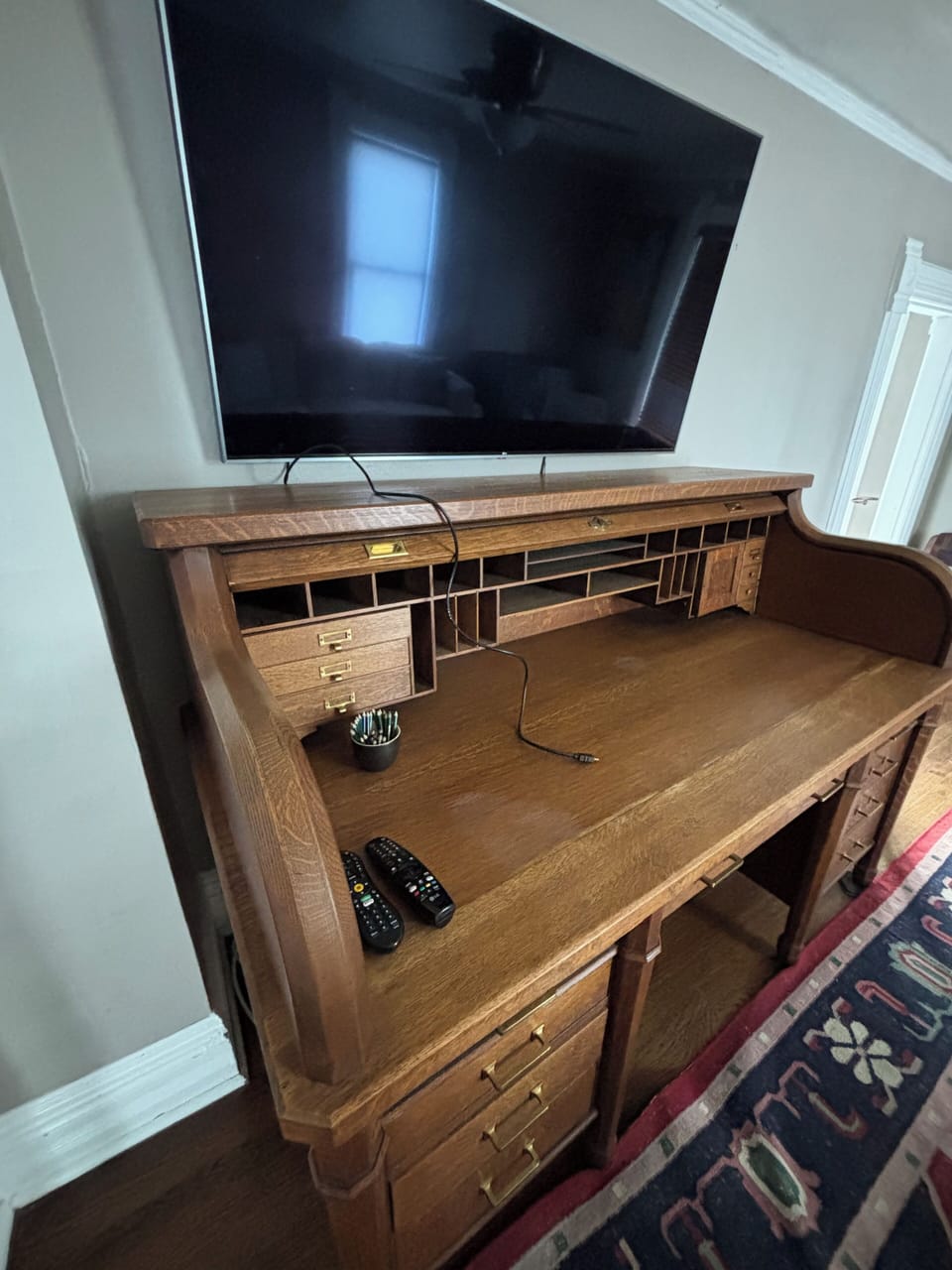 A high quality and nice size television with a USB cable above an antique desk.