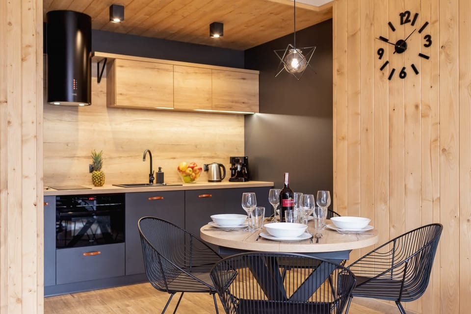 A compact yet stylish kitchenette with wooden finishes and modern black chairs arranged around a dining table.