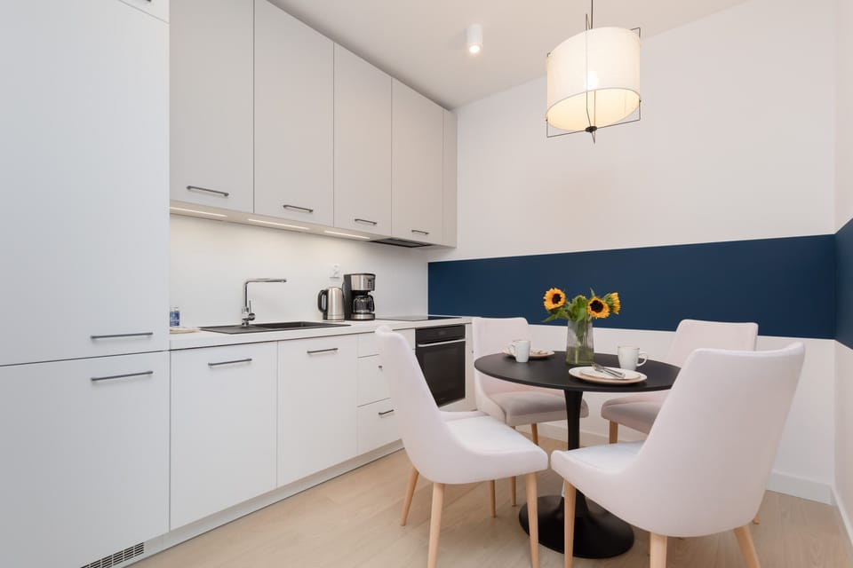 A modern kitchen with white cabinets, a dining table, and stylish lighting fixtures.