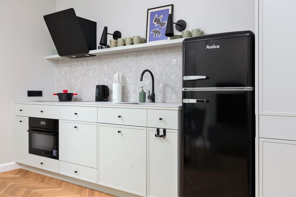A modern kitchen area with white cabinetry, a black fridge, and essential appliances.
