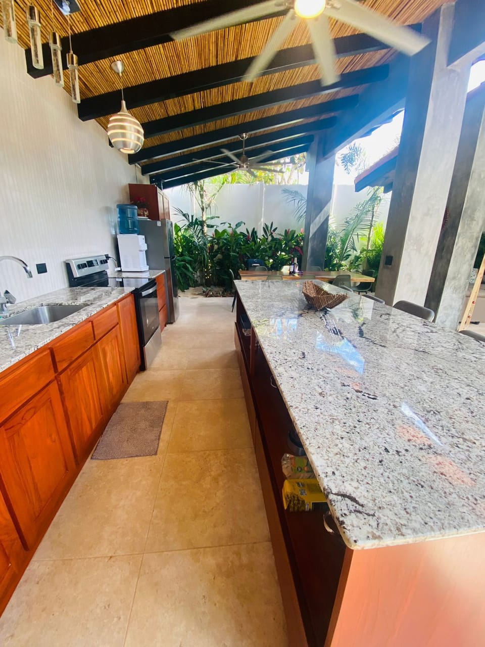 Spacious outdoor kitchen with granite countertops, ceiling fans, and pool views