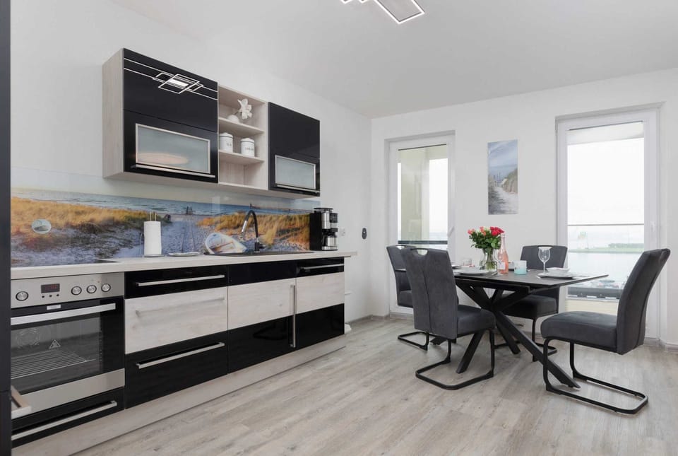 A modern kitchen with black cabinets, integrated appliances, and a bright dining area.
