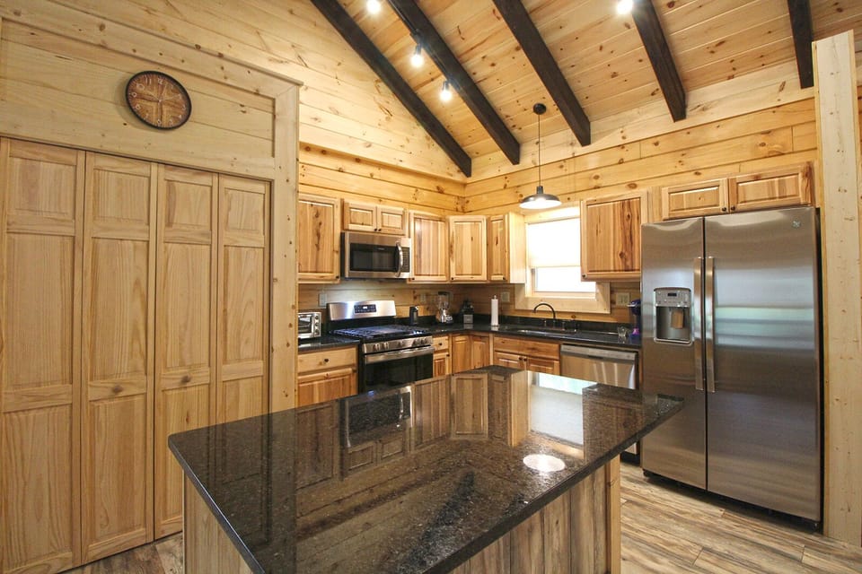 Fully equipped kitchen featuring granite countertops, custom wood cabinetry, stainless steel appliances, and center island seating.