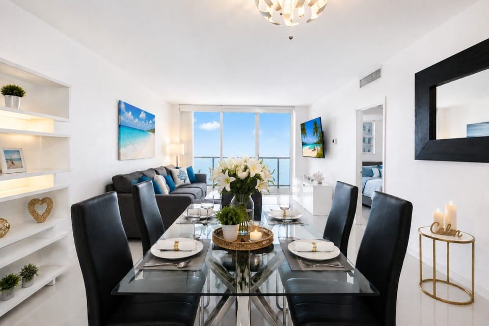 Elegant dining room with modern glass table seating 6 guests, contemporary black chairs, and sophisticated lighting. Perfect for family meals and special occasions with ocean views nearby.