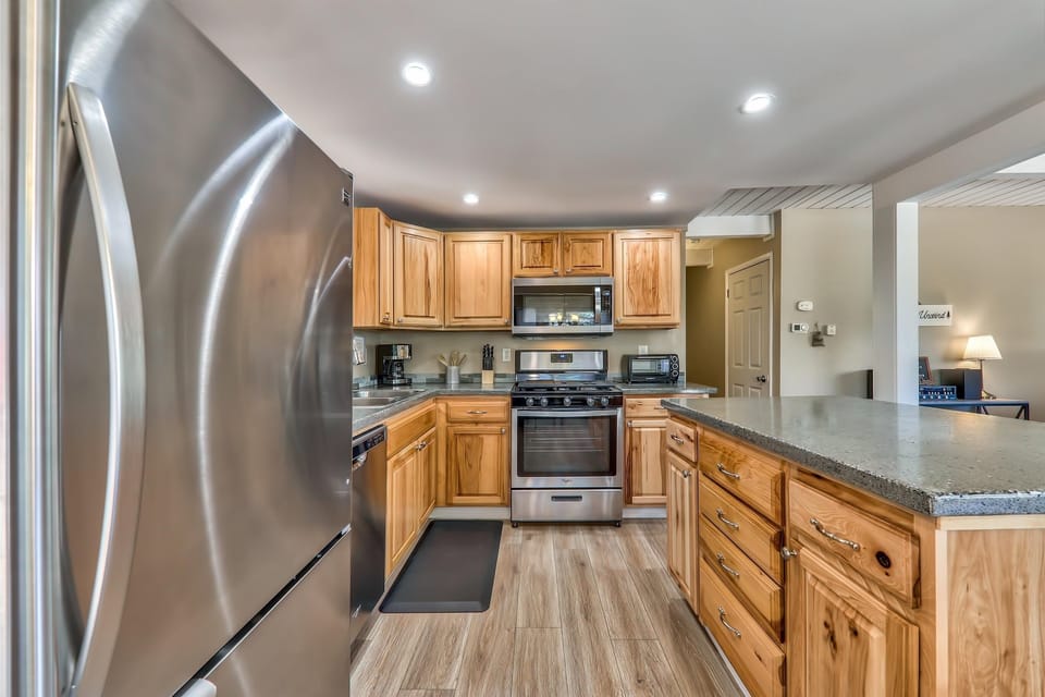 Kitchen with natural wood cabinets, stainless steel appliances, concrete-style countertops, and light wood plank flooring.