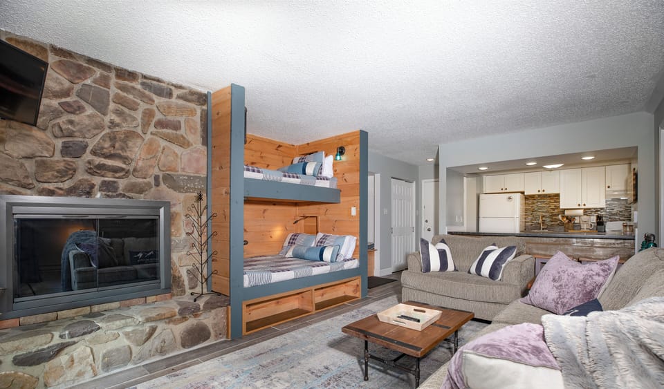 Living room w/ stone fireplace and built-in bunk beds w/ device chargers and reading lamps