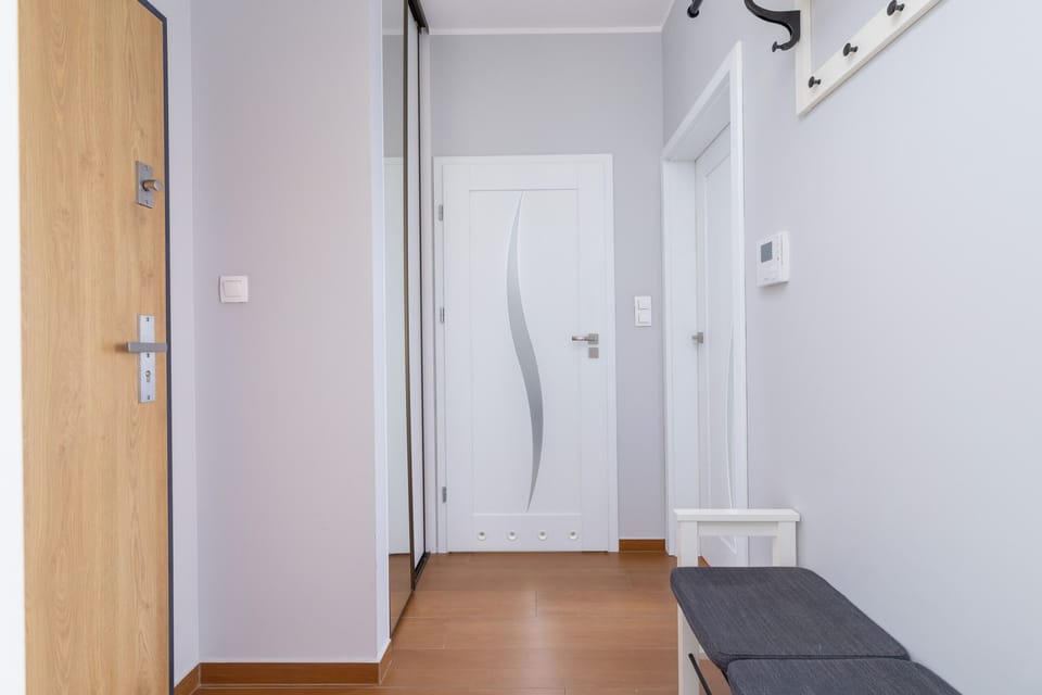 A minimalistic hallway with wooden flooring, white walls, and doors leading to different rooms.