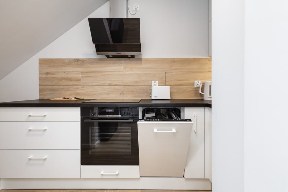 A modern kitchenette with white cabinets, a built-in oven, and a wooden backsplash.
