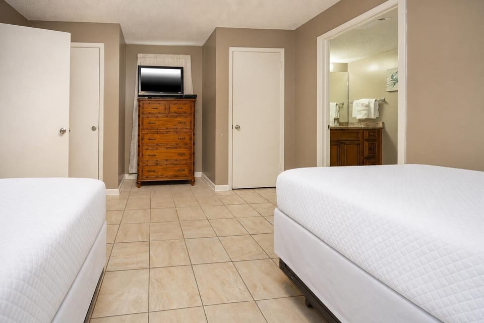 Cozy guest bedroom featuring two comfortable double beds, a wooden dresser, and a TV