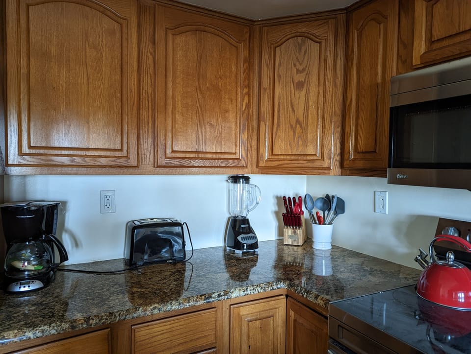 Kitchen with tea kettle, coffee pot, blender, toaster, and cooking utensils.