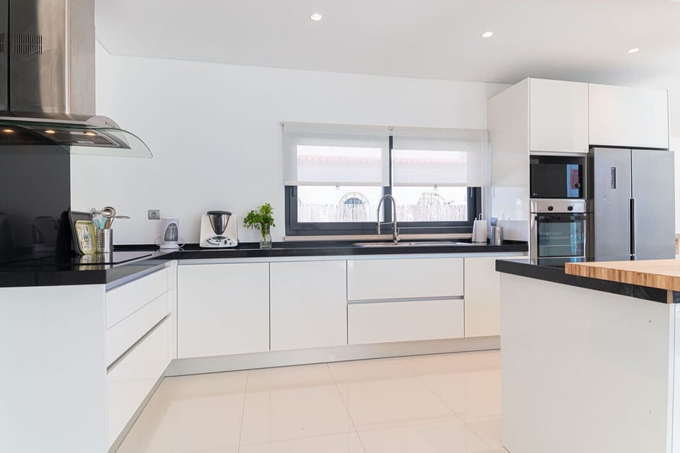 Modern white kitchen with black countertops and stainless steel appliances — Villa Melissa, luxury holiday villa in Grândola