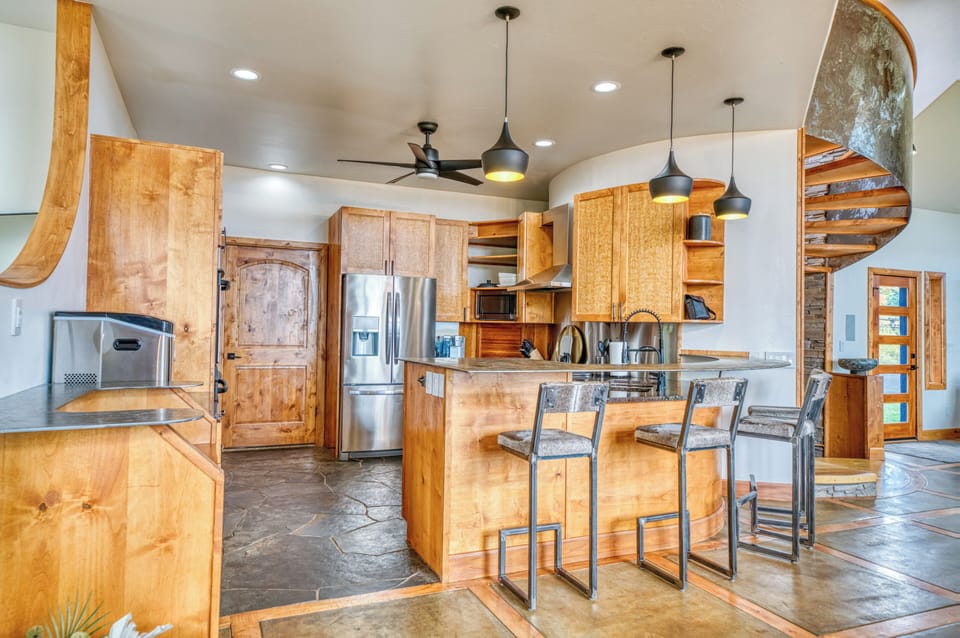 Modern kitchen with wood cabinets, bar seating, and a spiral staircase nearby.