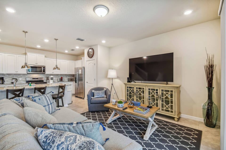 Relax in this cozy living area with a plush sectional in blue and white, complemented by a stylish coffee table. Enjoy your evenings by the large TV, all seamlessly connected to the modern kitchen for an airy feel.