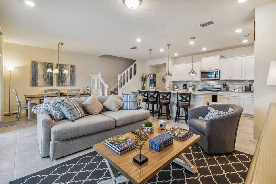 Welcome to a spacious living area with a plush gray sofa and chic rug, ideal for unwinding after your adventures. The open layout flows into a bright kitchen with modern cabinetry and stylish bar seating for your comfort.