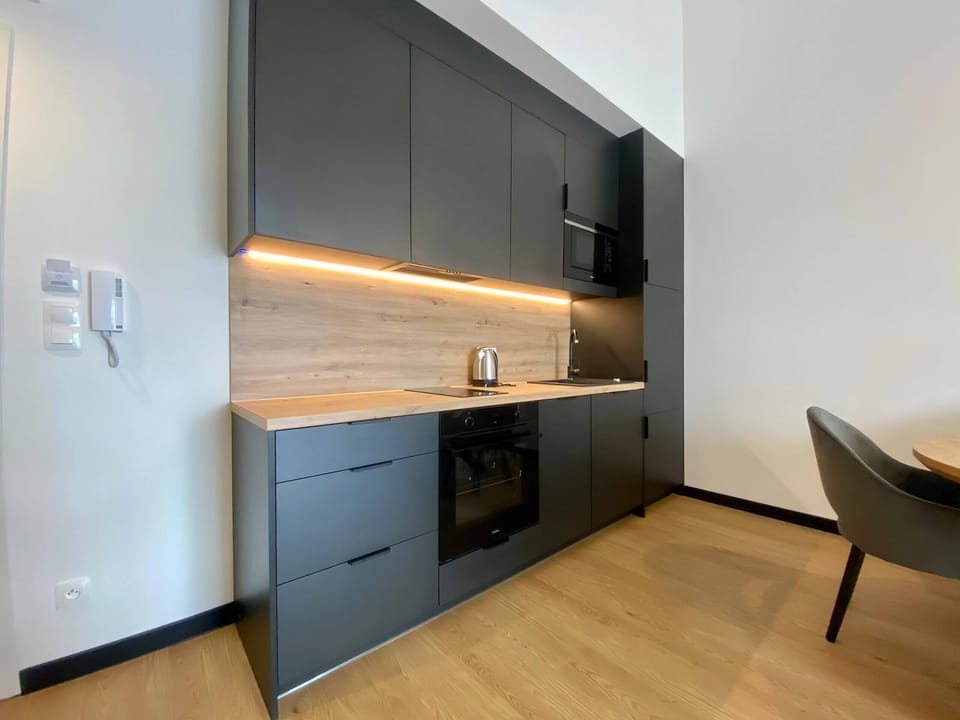 A sleek kitchen with black cabinetry, wooden accents, and under-cabinet lighting, offering functionality and elegance.
