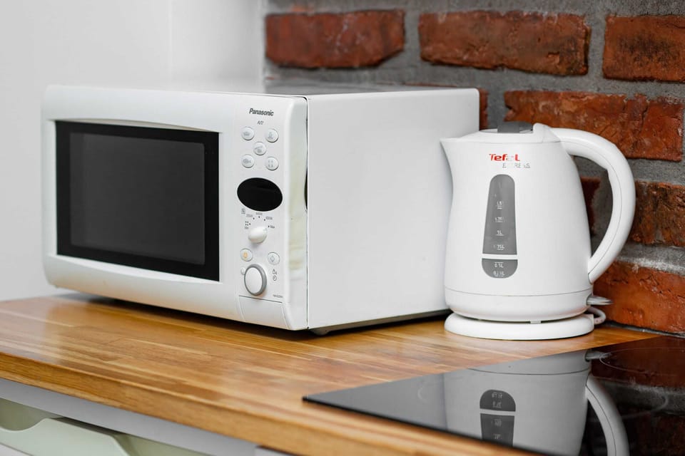 A kitchen counter with a microwave, kettle, and well-organized shelves for convenience.
