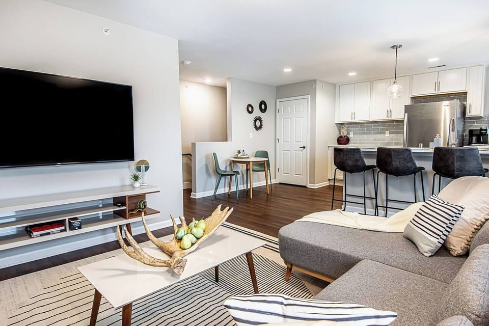 65 inch Google TCL TV. Entertainment stand with checkers, jenga, and a  deck of  cards.  Peninsula kitchen with 4 bar stools and a small table. 