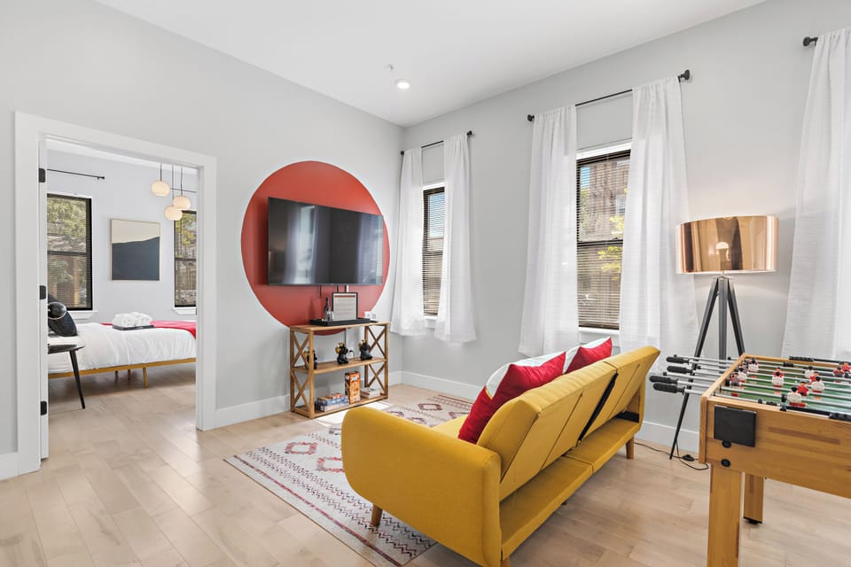 Welcoming living room flooded with natural light, featuring a state-of-the-art smart TV for entertainment, and a lively foosball table, creating a perfect space for relaxation and fun gatherings.




