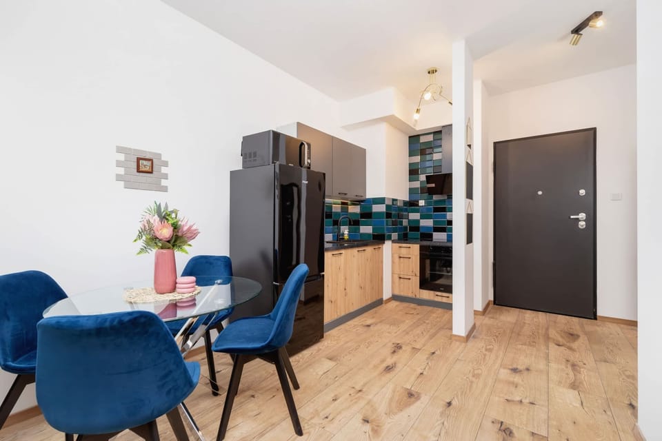A spacious living and dining space with blue accent chairs, wooden flooring, and a stylish kitchen in the background.
