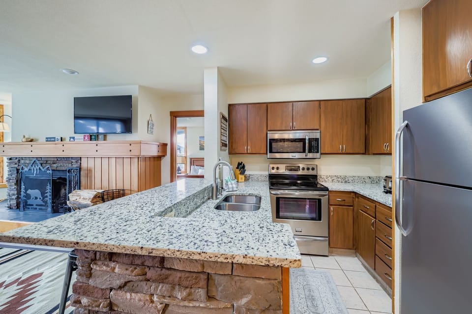 Your fully equipped kitchen features granite countertops, stainless steel appliances, and an open layout with a cozy fireplace - perfect for cooking meals and gathering together.