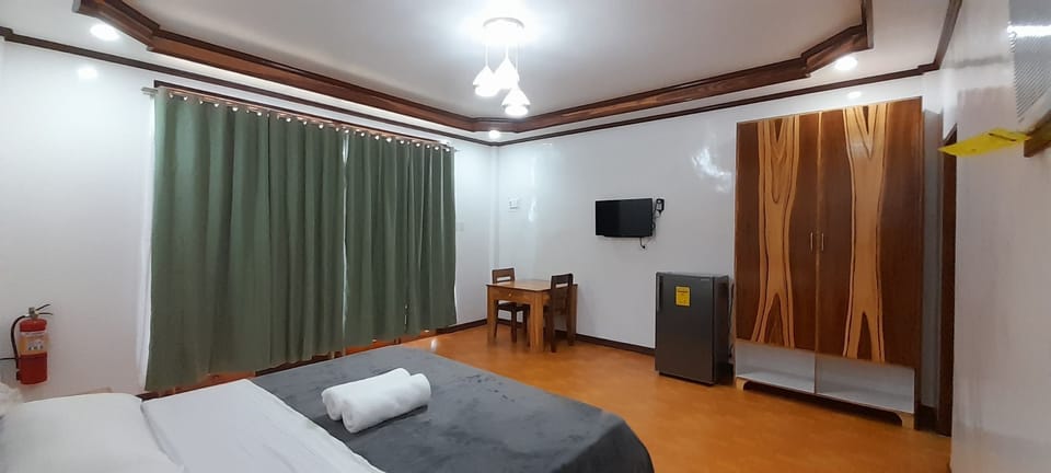 King size bed, blackout curtain closed, table & chairs, TV, Fridge, and closet.