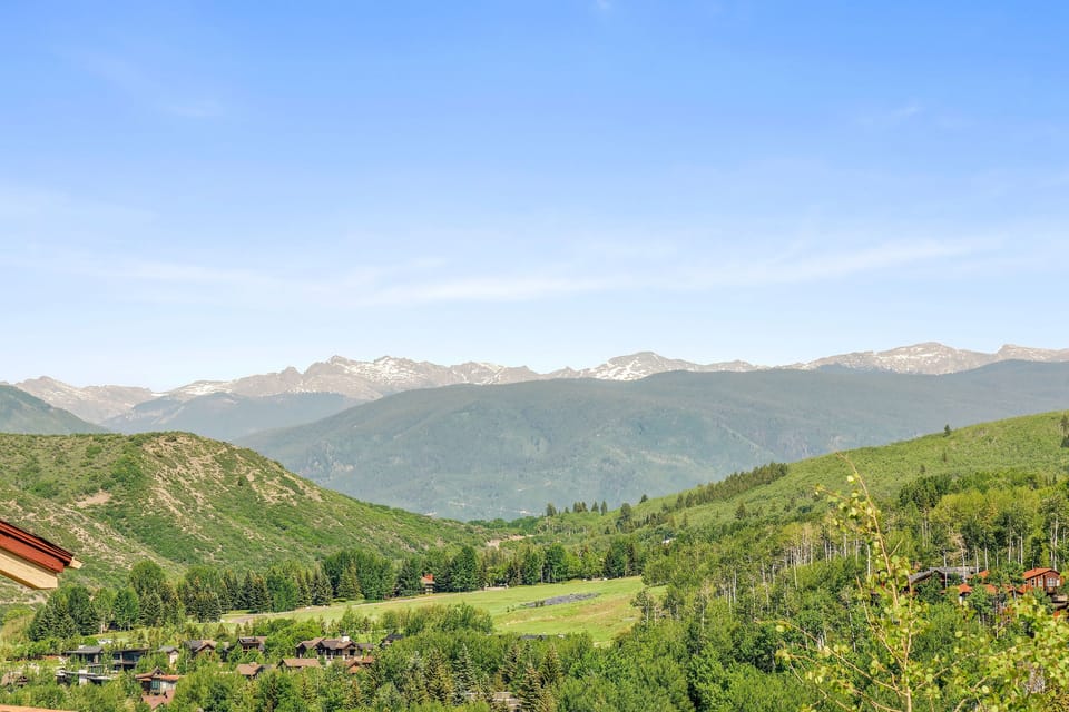 A picturesque landscape featuring verdant hills, scattered homes, and distant mountains under a clear blue sky.