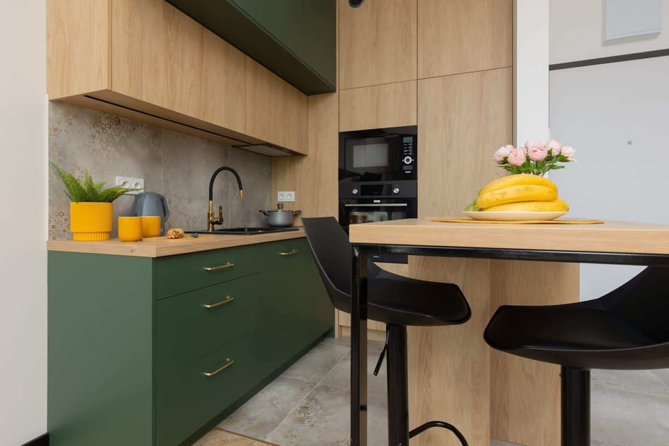 A modern kitchenette with green cabinets, wooden accents, and a small breakfast bar for convenience.
