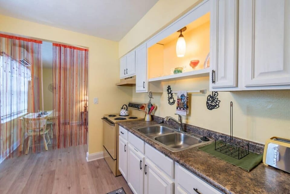Compact kitchen with white cabinetry and a double sink, leading to a dining area through a colorful curtain.