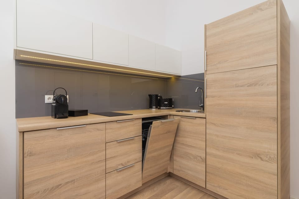 A stylish kitchenette with wooden cabinetry and a black countertop. It is equipped with essential appliances for convenient cooking.
