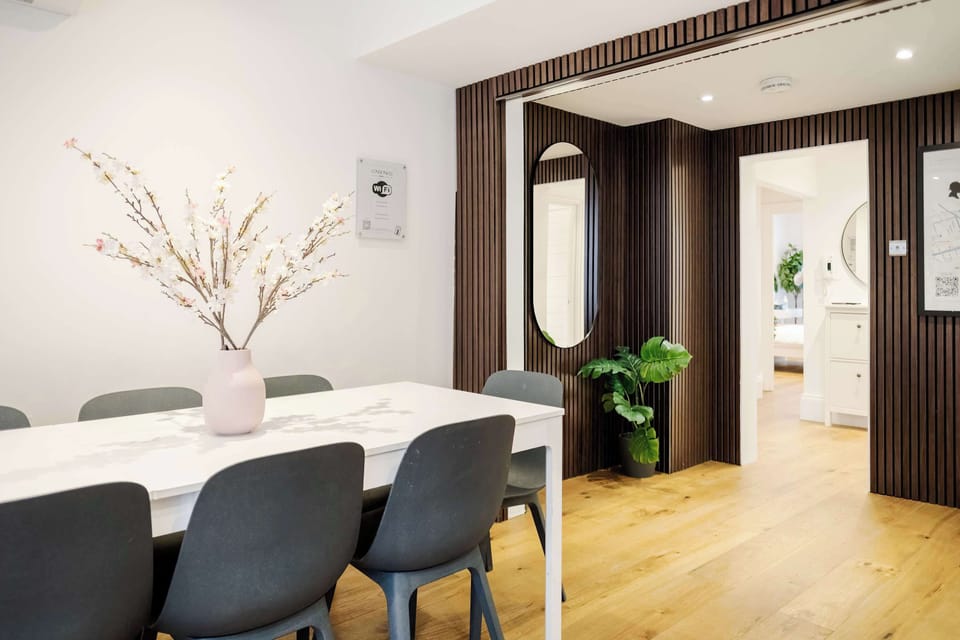 Living Room | A beautifully decorated and spacious living room featuring elegant wooden panels, a large 75 inch smart TV for relaxing evenings, and a dining table that comfortably seats up to 8 guests, perfect for meals and quality time together.