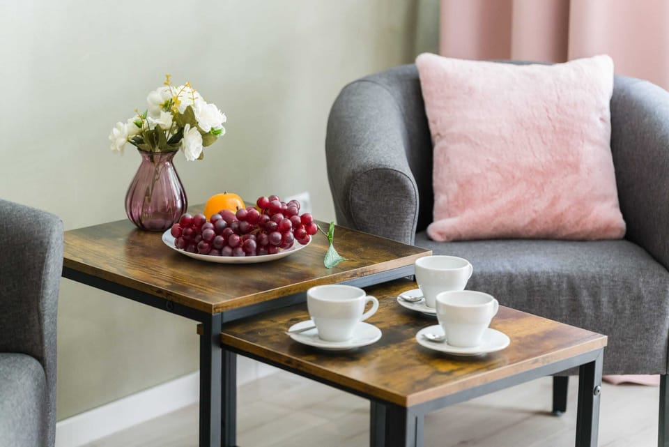 A close-up of a small coffee table with a cup of tea, a bowl of cherries, and a comfortable pink cushion in the background.
