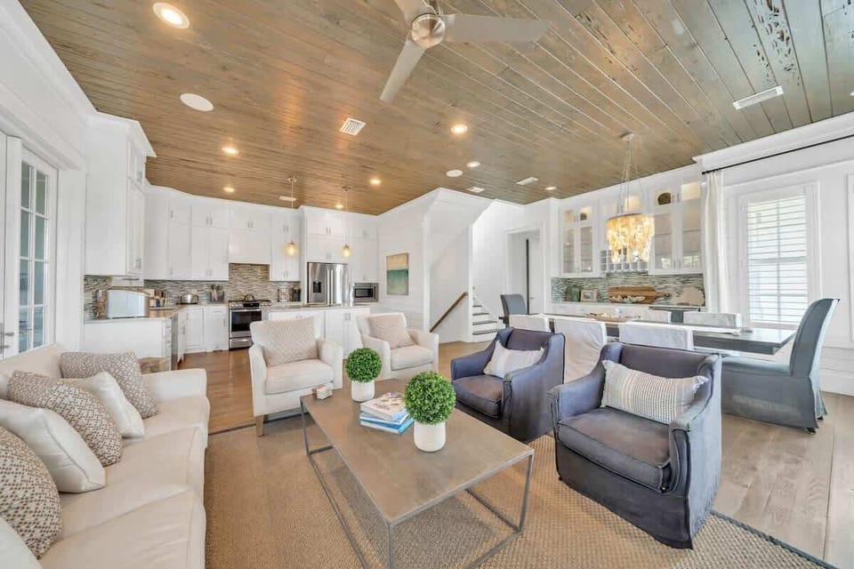 - Open plan design blends kitchen, dining, and living under a rustic wood paneled ceiling - Plush seating with neutral sofas and blue chairs offers a cozy space to unwind - Sleek kitchen features stainless appliances and a marble backsplash