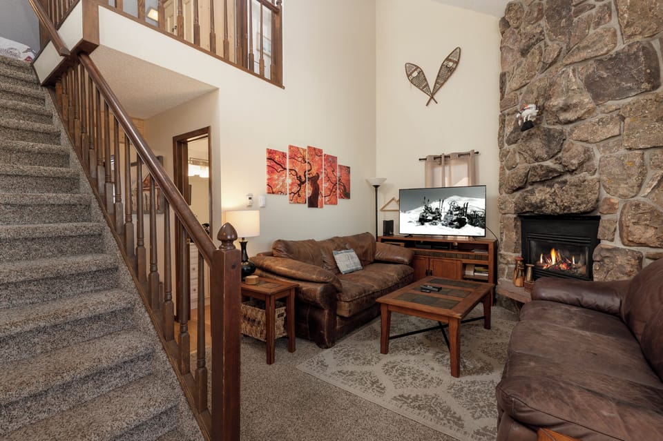 Cozy up in your spacious living room with warm leather seating, crackling stone fireplace, and rustic mountain charm perfect for relaxing evenings.