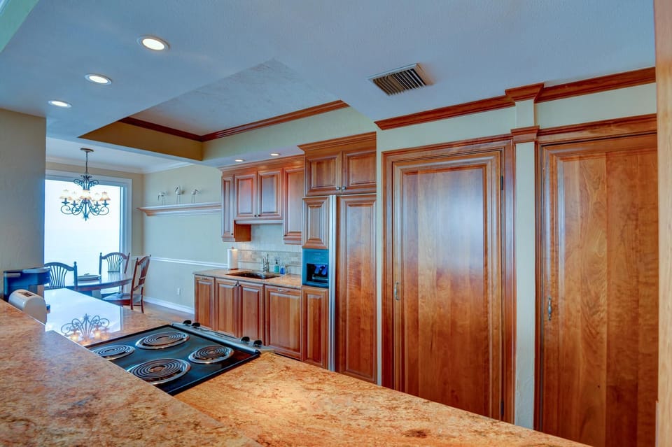 Cherry wood cabinetry and granite countertops frame the kitchen, with a built-in electric cooktop and adjacent dining area.