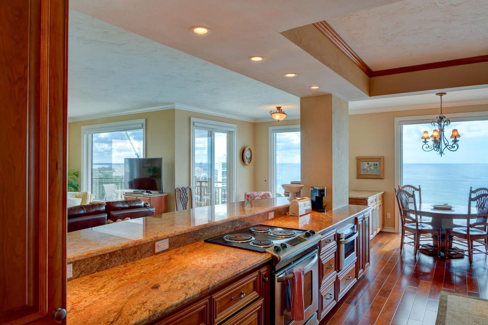 Granite breakfast bar separates kitchen from living room with leather sofas and TV near balcony doors.