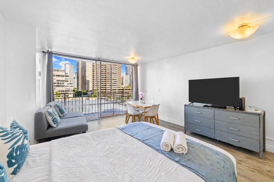 Bright studio with a queen bed, sofa, cute table, and private balcony with city views