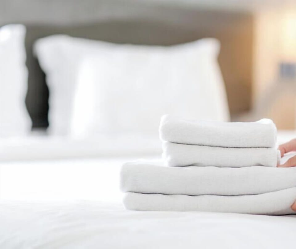 Your fresh linens are neatly prepared—crisp sheets on a plush bed and soft towels stacked and ready for your arrival, ensuring comfort from the moment you step in.