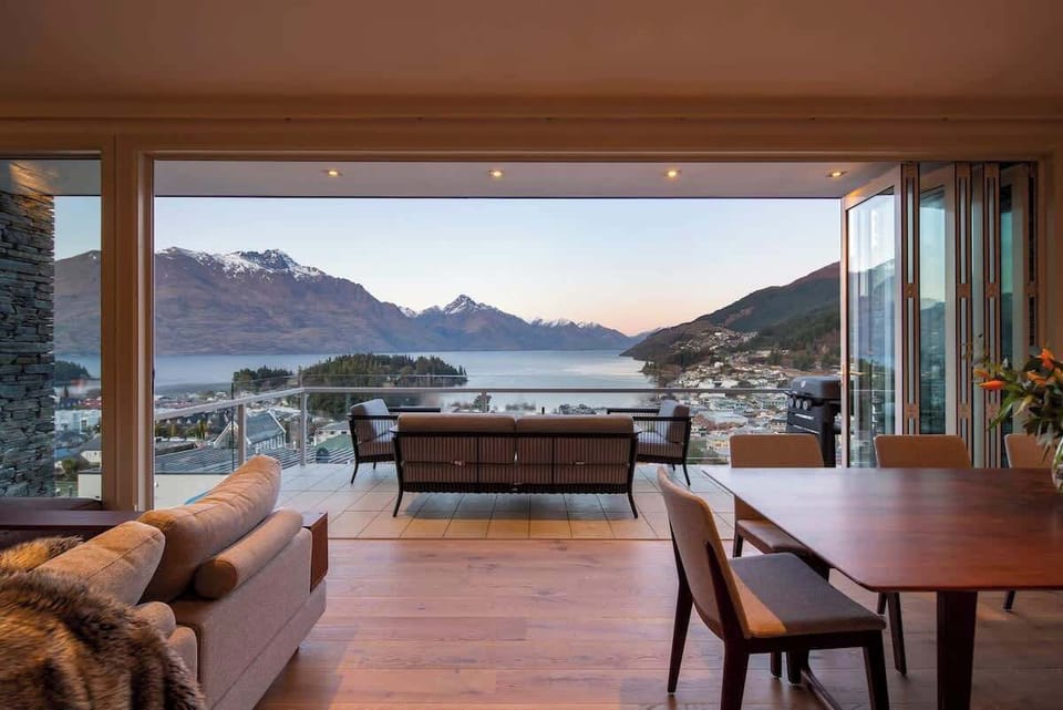 Living Room: Sun-drenched space with seating for five, gas fireplace, Smart TV, and sweeping lake and mountain views through floor-to-ceiling windows.