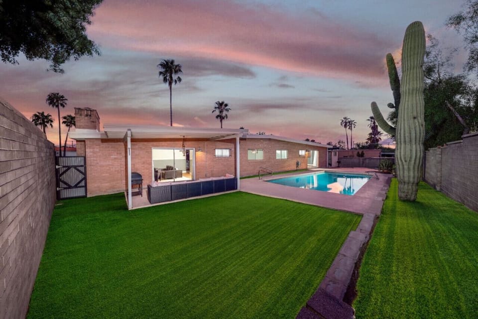 The whole backyard at golden hour — pool (unheated), grassy lawn, and a cozy patio with seating and grill