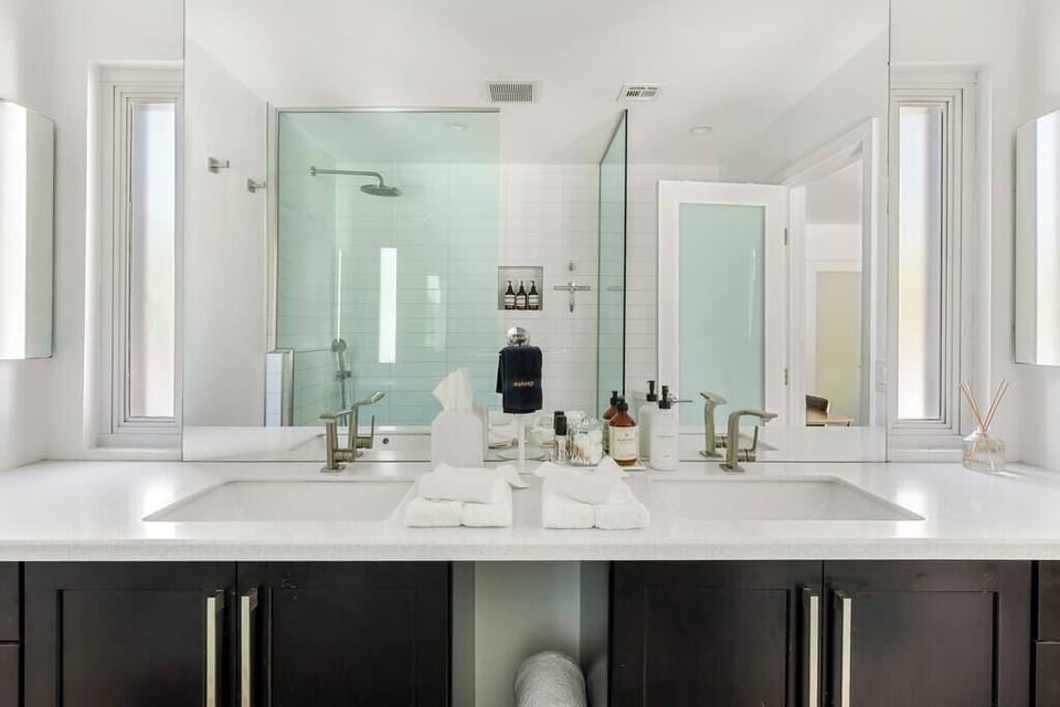 Bright primary bath - dual vanity with quartz counters, glass-enclosed rain shower, dark wood cabinetry. Hotel-level amenities at home.