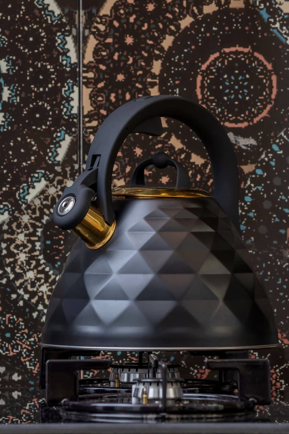 A modern kettle with a textured design and a patterned backdrop.
