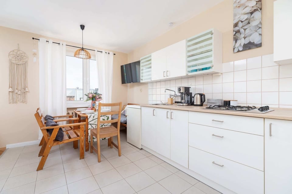 A kitchen area with a dining table and chairs, white cabinets, and natural lighting from the windows.
