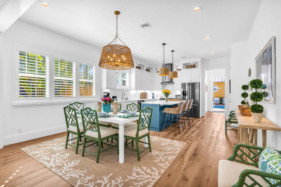 The dining area is unique with its bright green dining chairs, frosted glass-topped table, and seating for 8. Towering above is an eye-catching basket light fixture. The open plan dining area sits between the living room and kitchen.