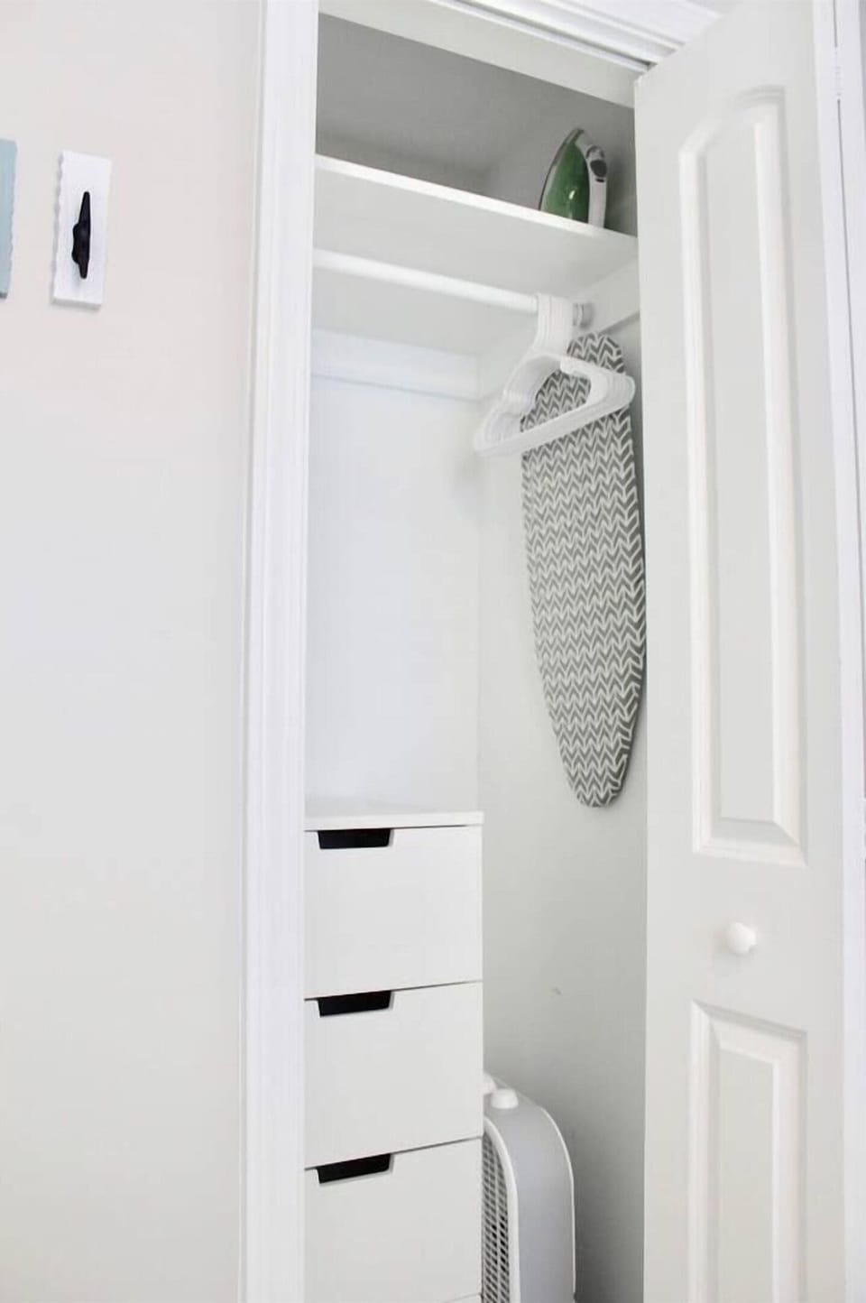 Efficiency dresser, hangers, box fan, iron, and ironing board located in master bedroom closet