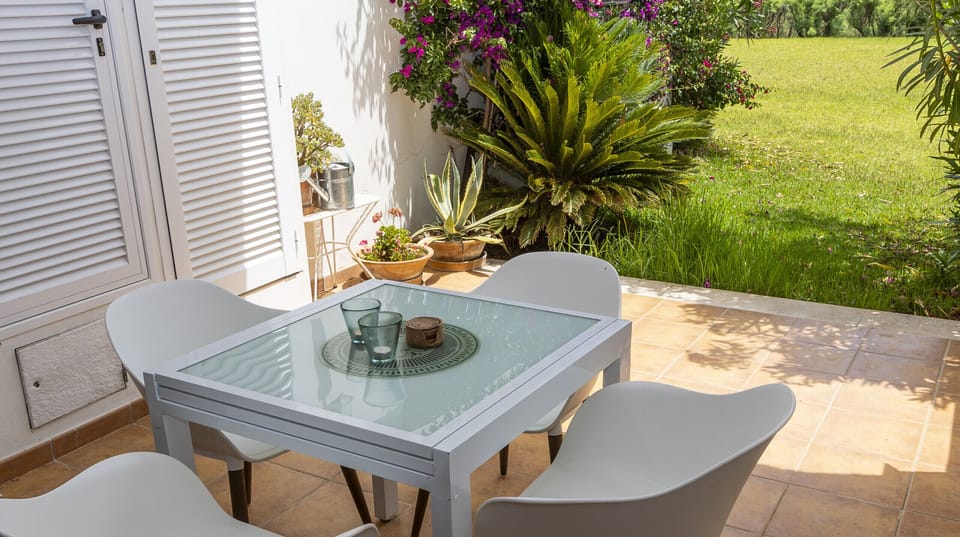 Outdoor terrace with glass table and chairs beside a garden with Mediterranean plants.